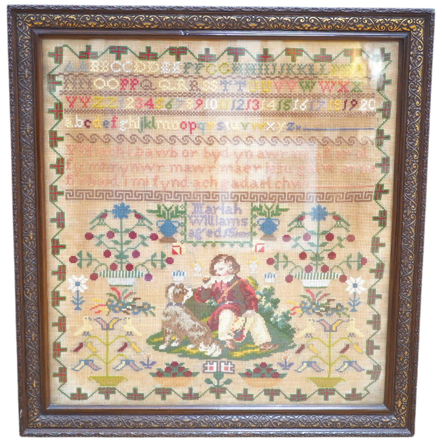 A 19th century cross stitch sampler by Mariah Williams age 15 dated 1879, worked with an outer geometric border, with rows of various alphabet letters and numerals., the lower half with large spot motifs of flowers, tree